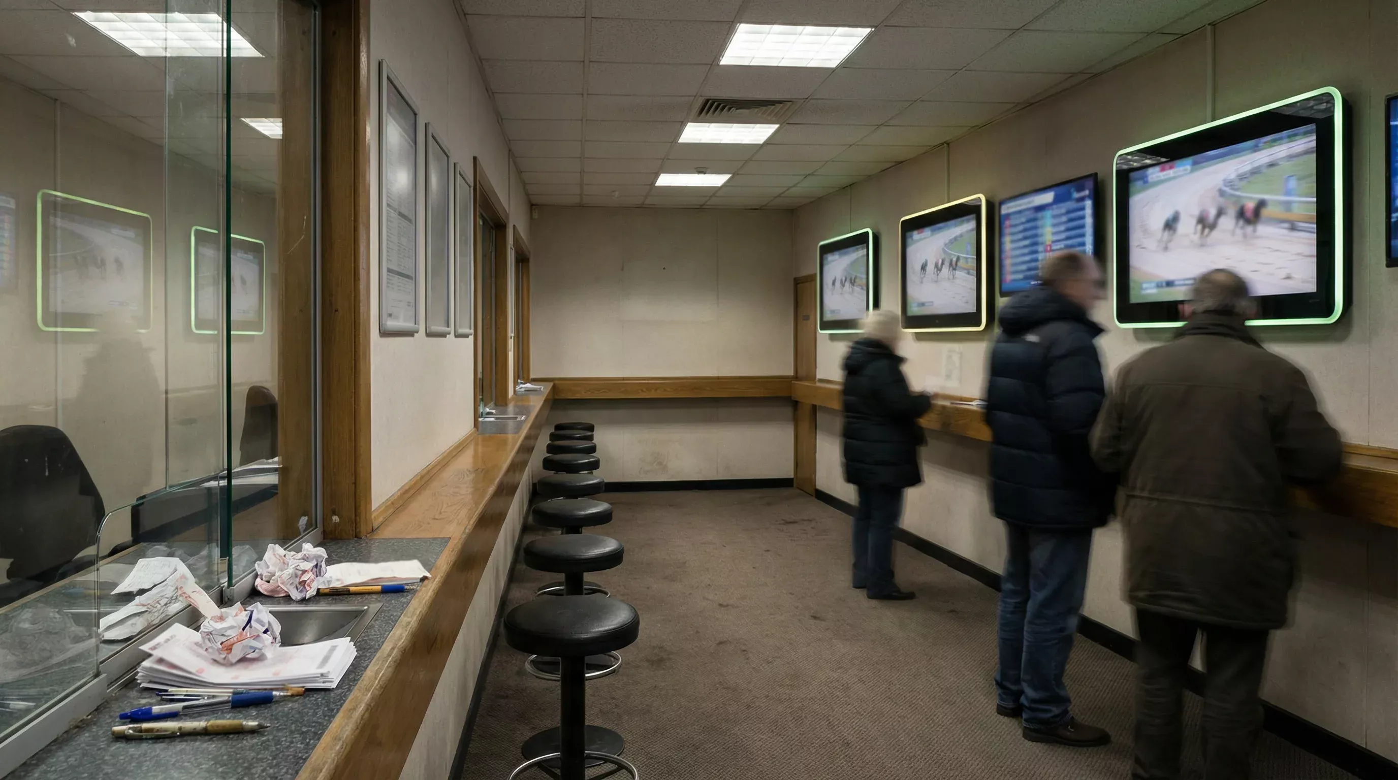 Interior of a UK betting shop with screens showing live greyhound racing from a sand track