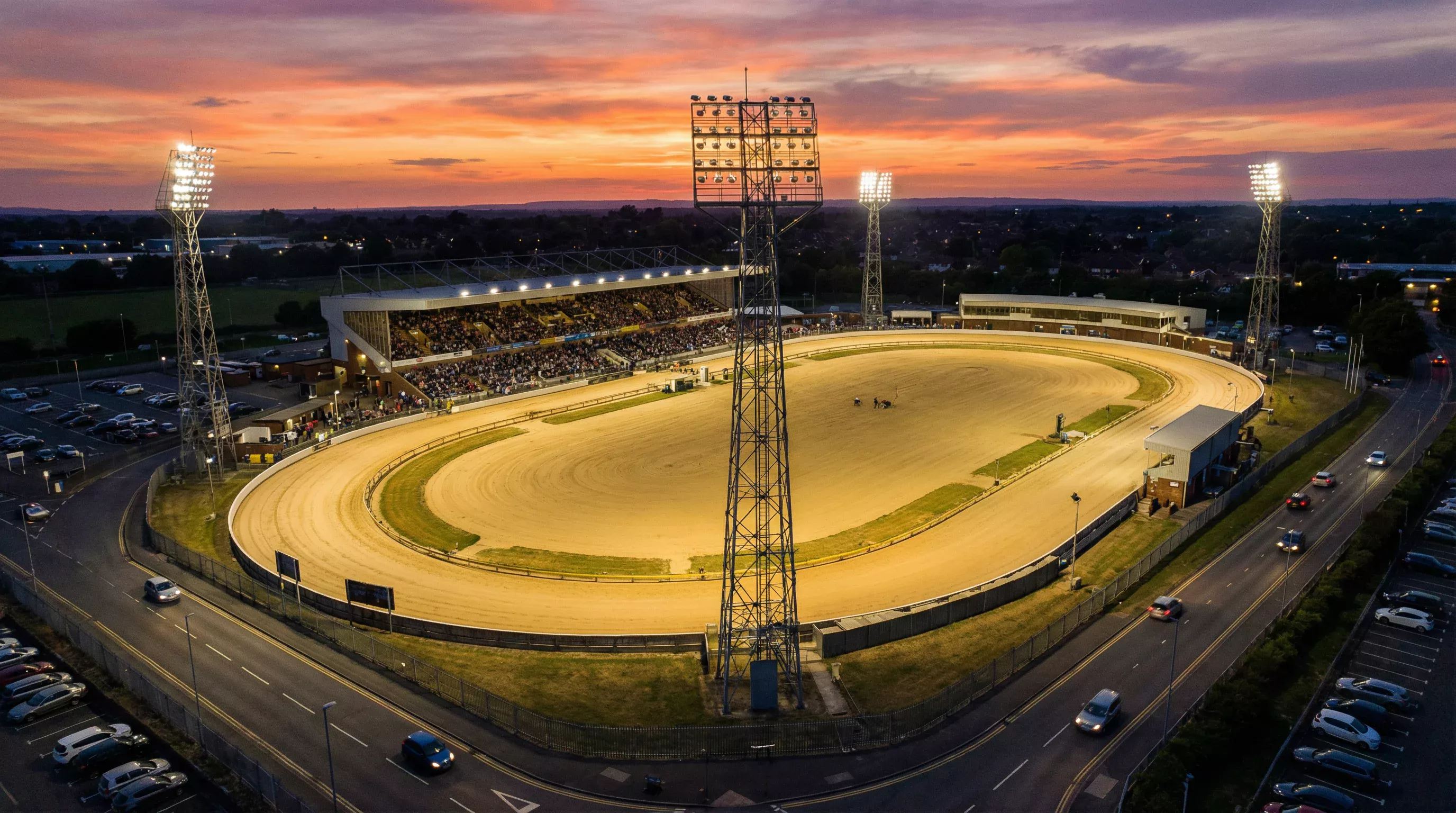 Aerial view of a greyhound racing stadium showing the oval sand track and grandstand at dusk