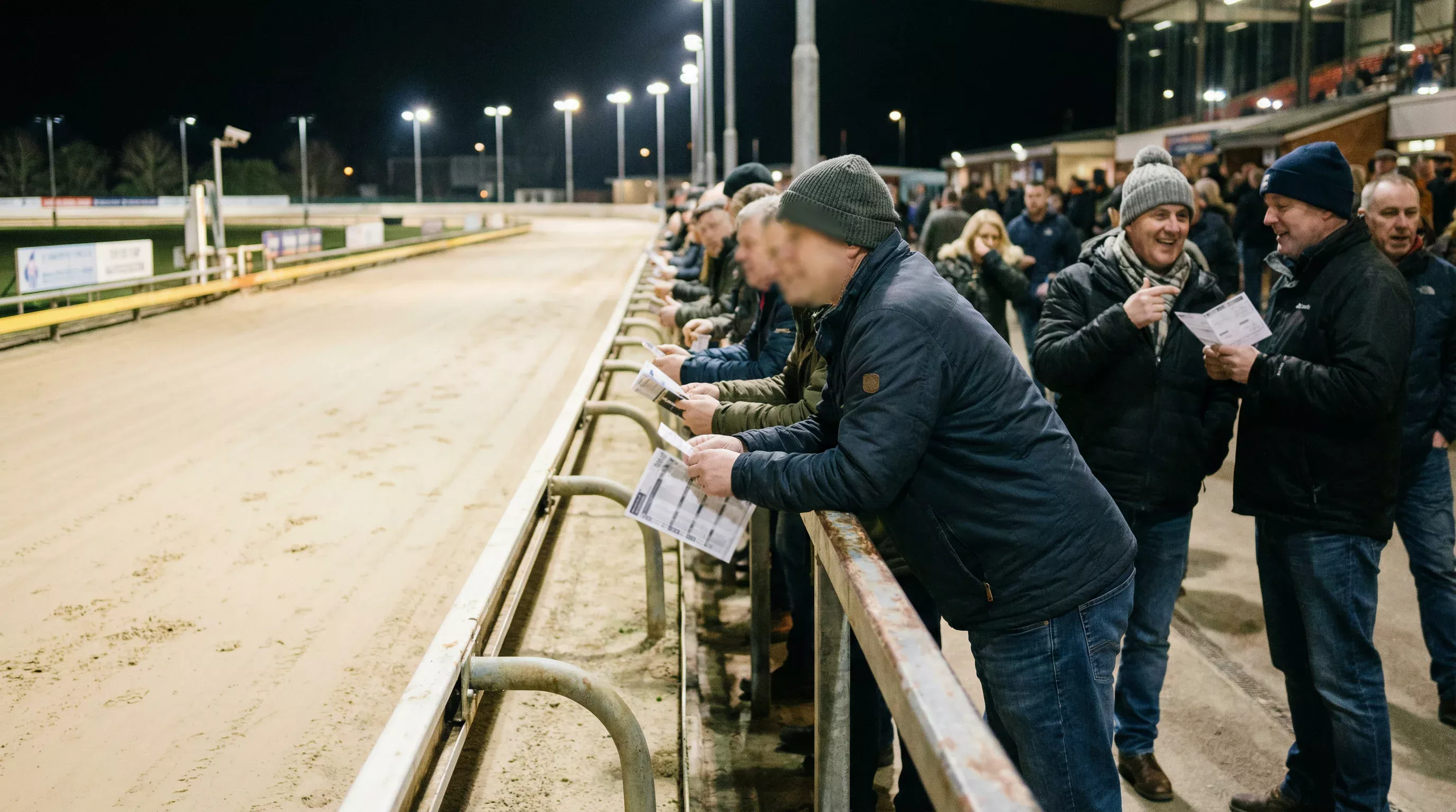 Crowd of spectators watching greyhound racing from the grandstand rail at Sunderland Stadium on a Friday night
